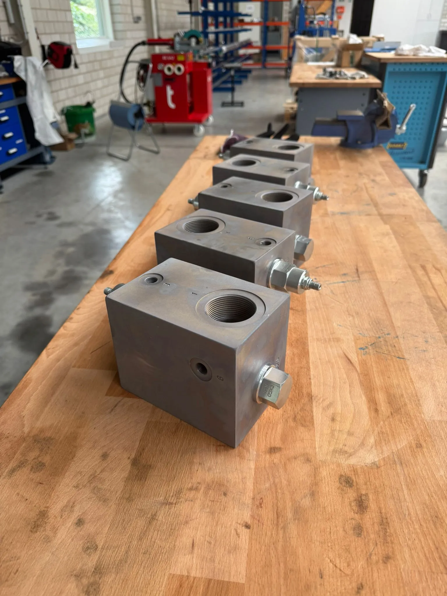 Fünf fertige Druckminderblöcke aus Sphäroguss nebeneinander auf der Werkbank in der Halle von FPS Hydraulik in Holdorf, mit eingeschraubten Sun-Cartridgeventilen und Verschlussstopfen