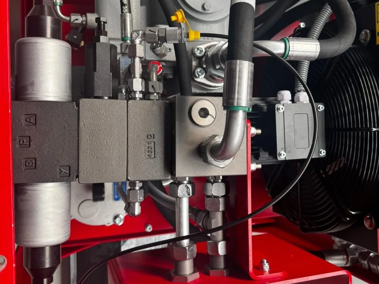 Ventilstapel mit gekennzeichneten Anschlüssen A, P, B und T auf einem Steuerblock, daneben Hydraulikspeicher und Ölkühler in einem von FPS Hydraulik gebauten Aggregat